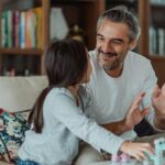 a girl holding toys while looking at her smiling father