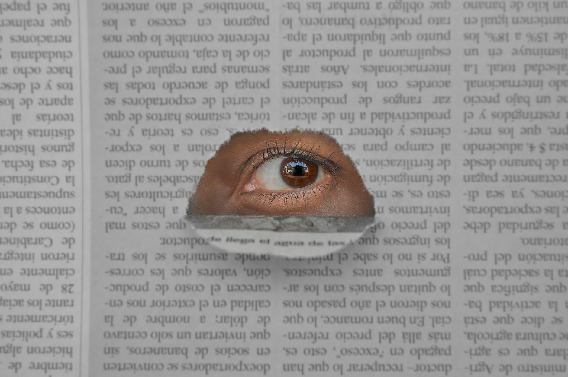 a brown eye on the hole of a newspaper