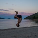 man performing flip on beach at sunset
