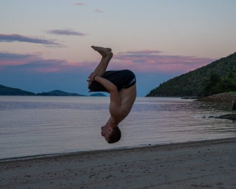 man performing flip on beach at sunset