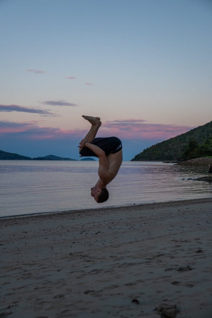 man performing flip on beach at sunset