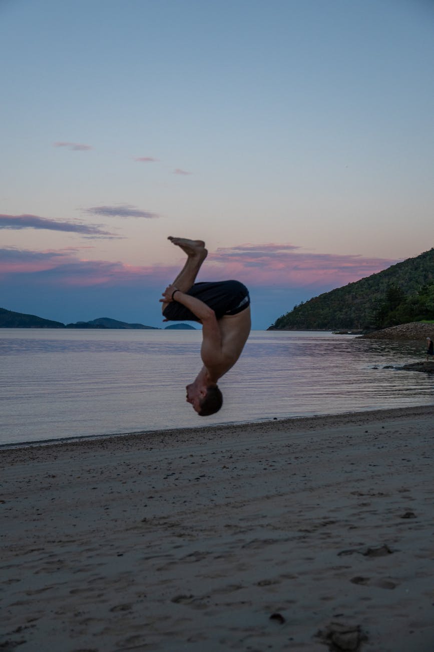 man performing flip on beach at sunset