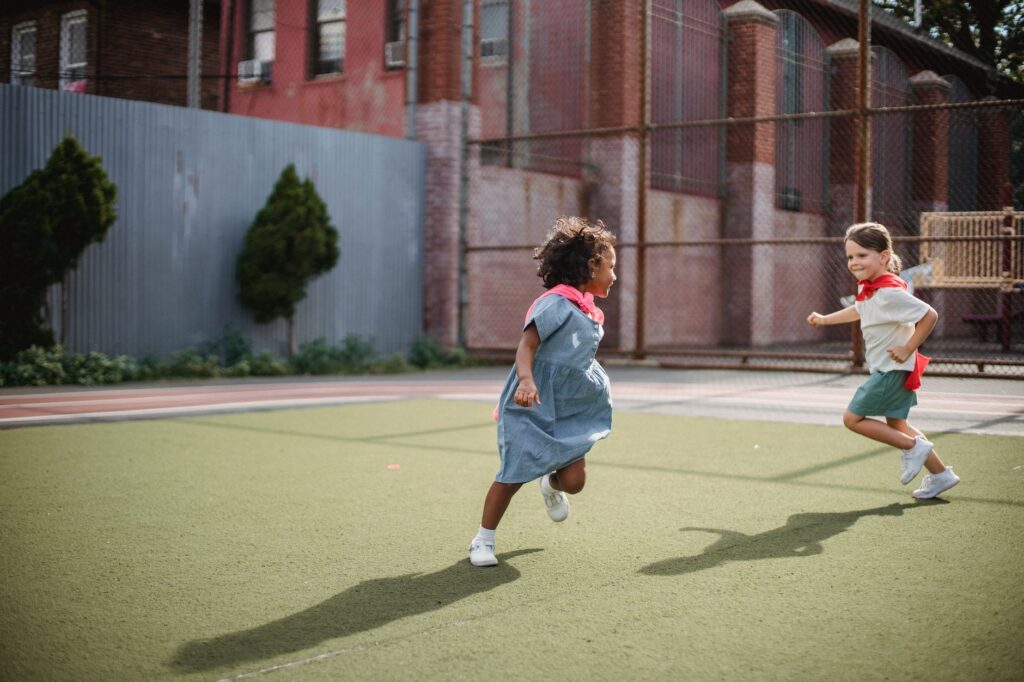 little girls running around a court in superhero capes