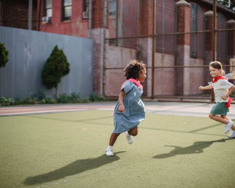 little girls running around a court in superhero capes